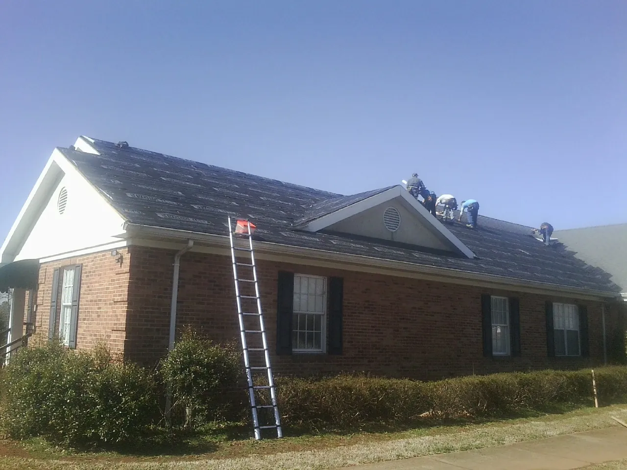 Crew tearing shingles off a brick ranch roof with a ladder set — Metal Roof Repair work by our crew in Wheaton