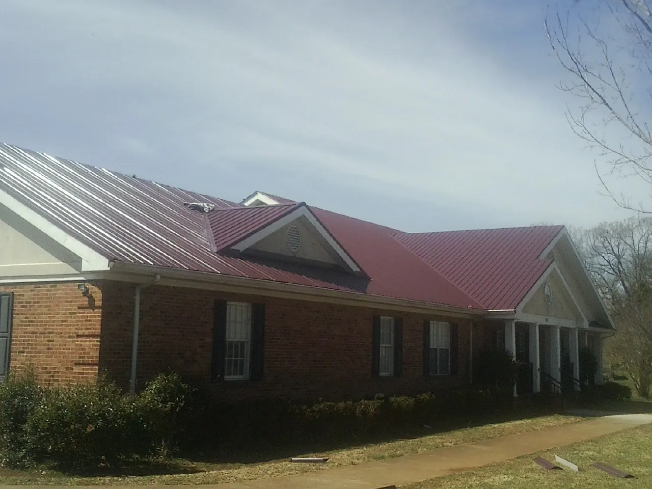 Red metal roof with gabled entries on a long brick building, from a Hail Damage Roof Repair job in Wheaton