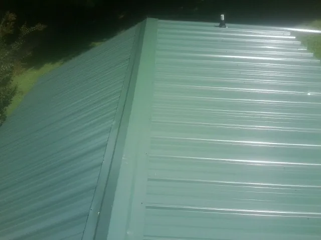New green metal panels meeting at the ridge of a roof — Flat Roof Repair work by our crew in Wheaton
