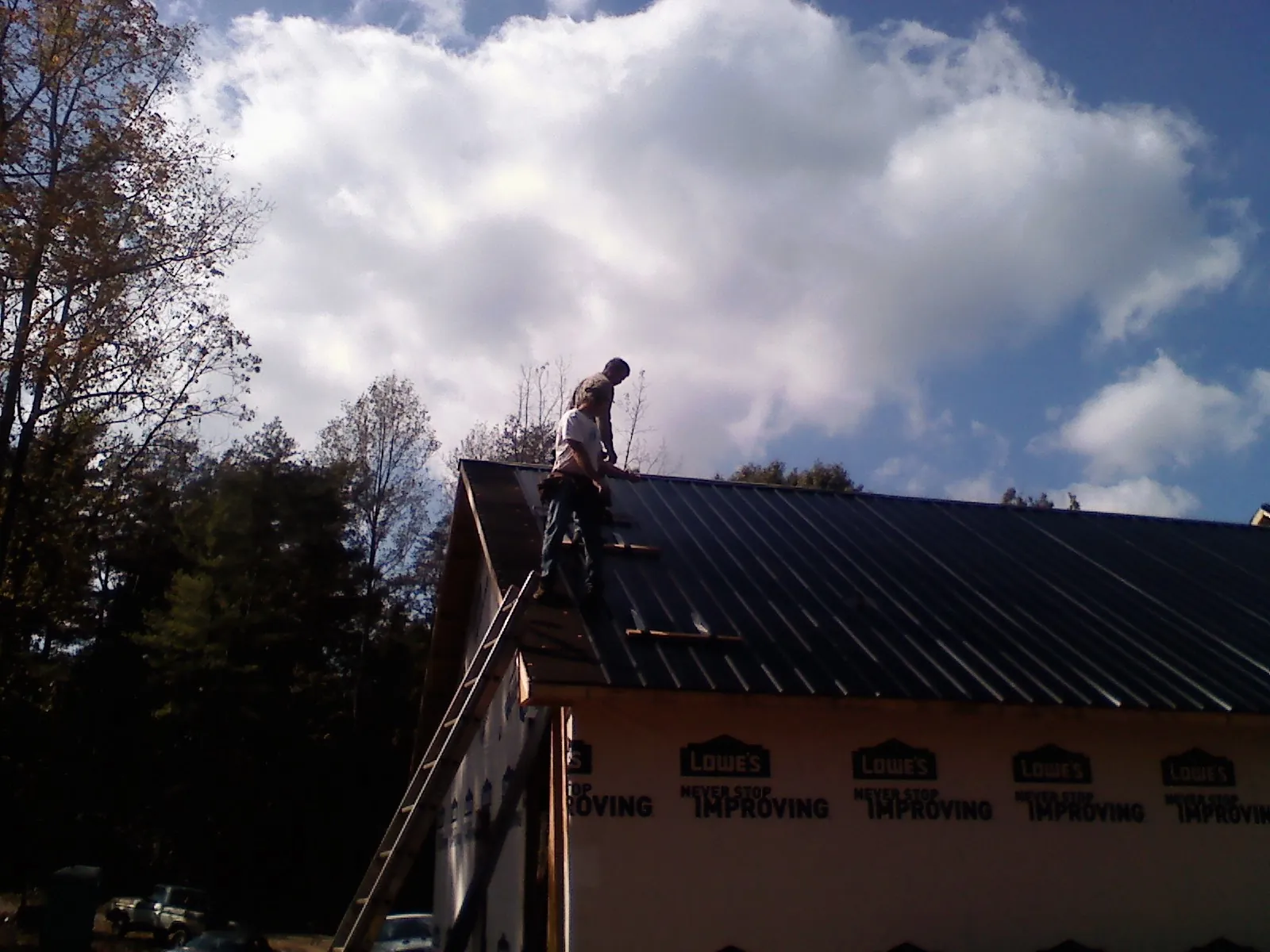 Roofer fastening dark metal panels high against a cloudy sky, from a Roof Inspection job in Wheaton